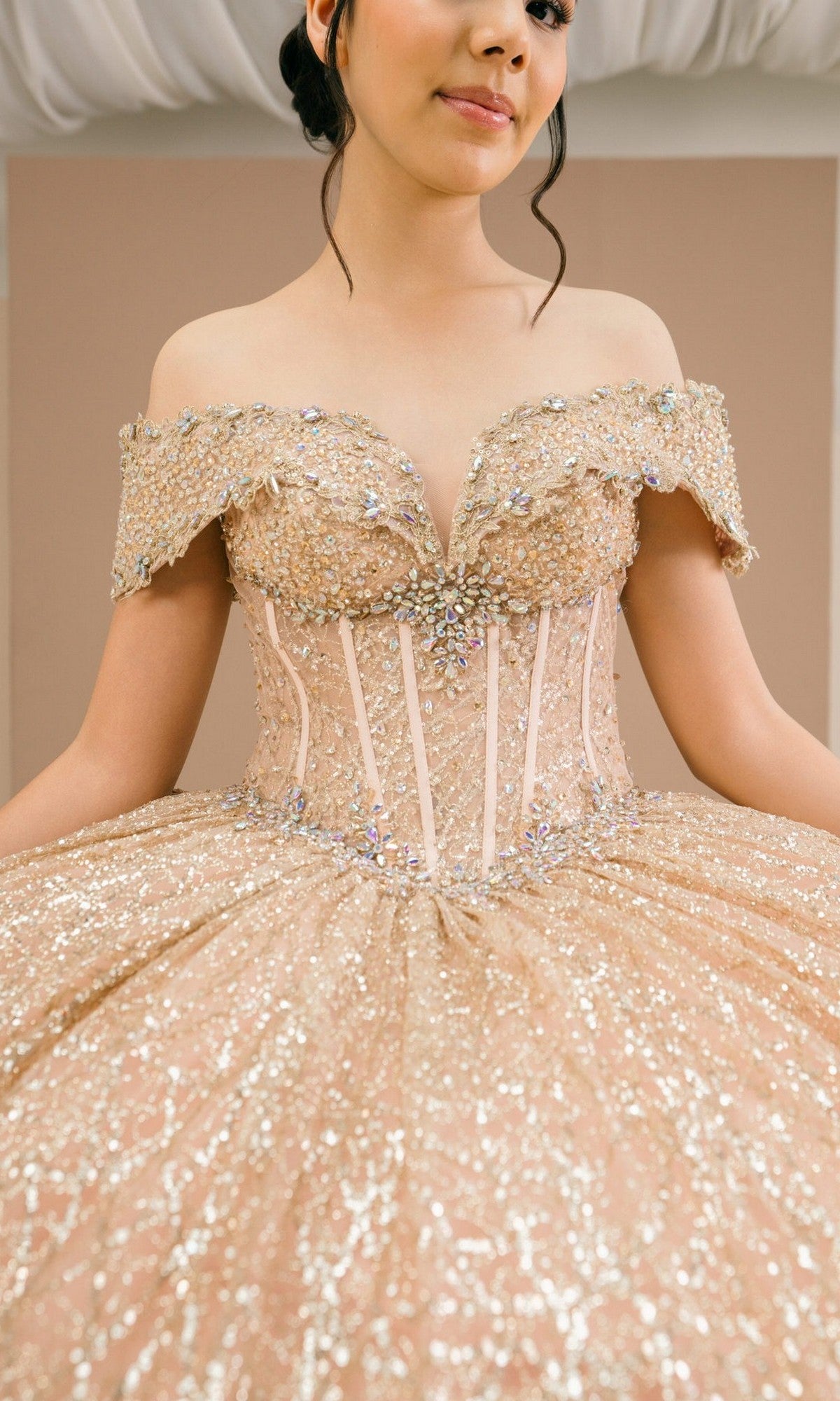 A young woman wearing the Quinceanera Dress 8600JQ by Cinderella Couture, a gold ball gown with an off-the-shoulder neckline, sparkling jeweled embellishments, and a fitted corset bodice.